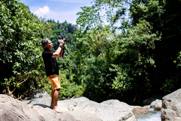 istock senior Asian photographer standing in jungle 1357687755