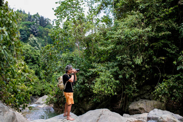 istock senior Asian photographer standing in jungle 1357687774