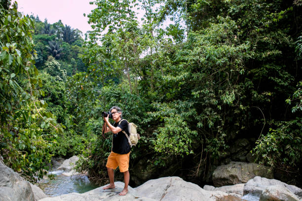 istock senior Asian photographer standing in jungle 1357687783