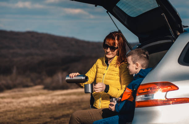 istock Mother and son take break from driving sitting by the car while drinking tea in nature. 1357689007