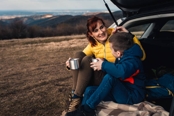 istock Mother and son take break from driving sitting by the car while drinking tea in nature. 1357690272