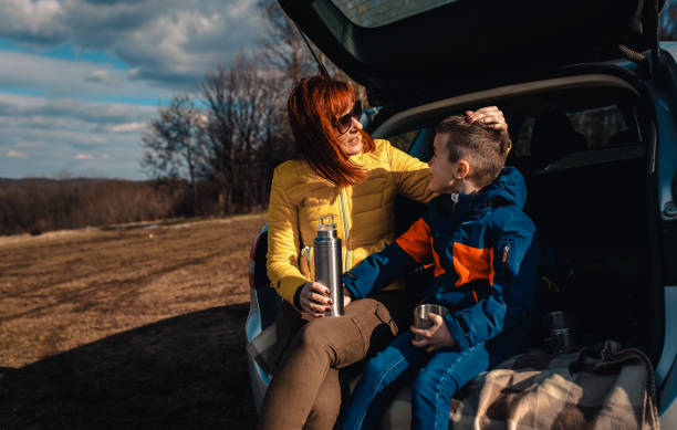 istock Mother and son take break from driving sitting by the car while drinking tea in nature. 1357690440