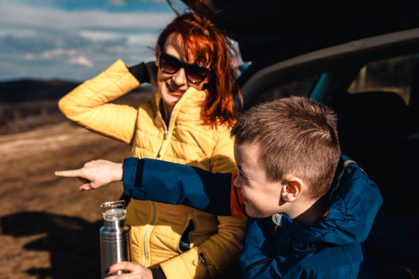 istock Mother and son take break from driving sitting by the car while drinking tea in nature. 1357690647