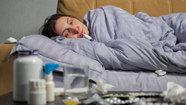 istock Sick woman measures temperature lying on sofa 1357690959