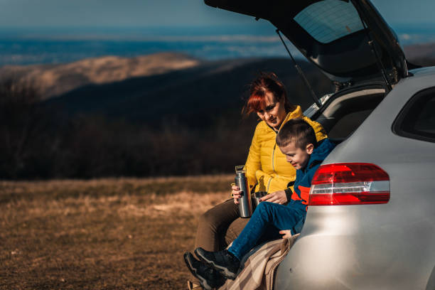 istock Mother and son take break from driving sitting by the car while drinking tea in nature. 1357691002