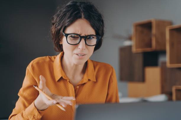 istock Frustrated Spanish female freelancer looking angry on laptop screen while working from home 1357693389