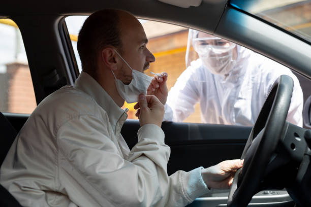 istock A man wearing a protective suit, gloves, surgical mask, and face mask is testing the coronavirus co id-19 on another man sitting in a car. 1357693698