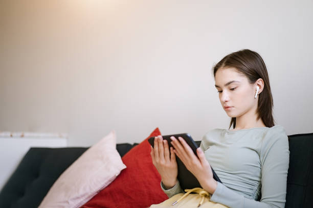 adolescente usando tablet em casa enquanto senta no sofá - distance running audio - fotografias e filmes do acervo