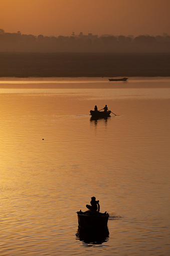 Varanasi, India - April 8, 2010: Silhouette of fishers sailing in fishing boats  on Ganges River, during sunset, Varanasi, India