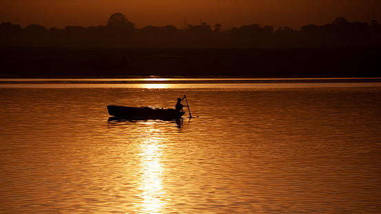 Varanasi, India - April 8, 2010: Silhouette of fishers sailing in fishing boat  on Ganges River, during sunset, Varanasi, India