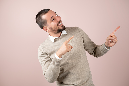 Young handsome man is pointing at copy space with his fingers in front of pink background.