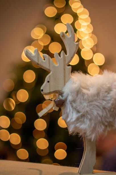 istock White cute and funny reindeer, christmas tree in background, bokeh, lights. 1357697459