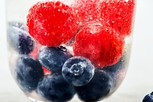 Blueberry and raspberry in glass with cold soda water drink, photographed through dewy glass.