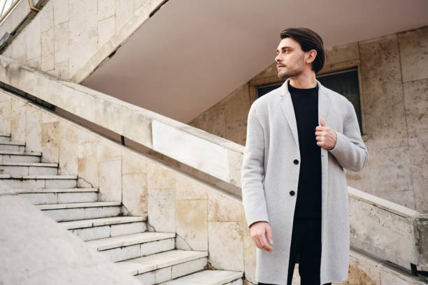 Young attractive stylish man in coat thoughtfully looking away on street Young attractive stylish man in coat thoughtfully looking away on street mens fashion stock pictures, royalty-free photos & images