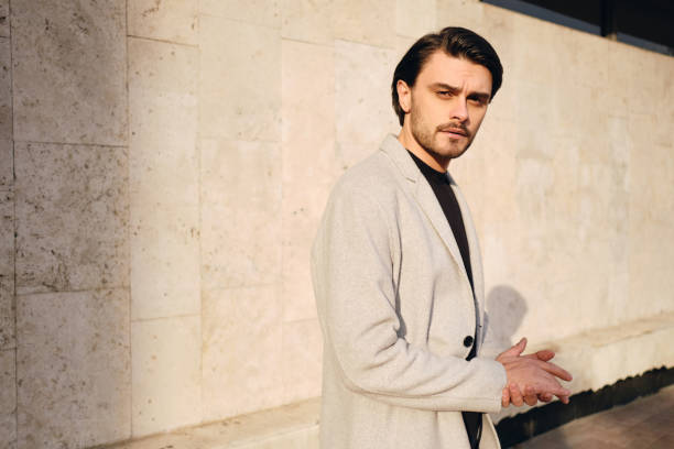 istock Young handsome stylish man in coat intently looking in camera outdoor 1357707821