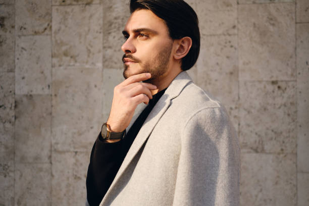 Side view of young handsome stylish man in coat thoughtfully looking away outdoor Side view of young handsome stylish man in coat thoughtfully looking away outdoor men fashion model stubble serious stock pictures, royalty-free photos & images