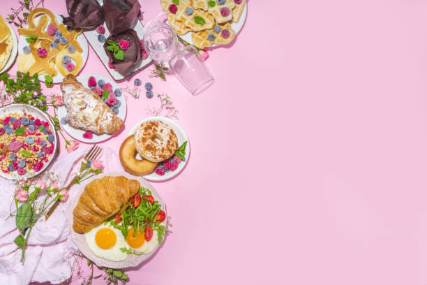 Valentine day brunch menu background with various breakfast and lunch dishes, waffle, croissant, muffins, donuts, berries, fries scrambled eggs, pancakes, pink background copy space