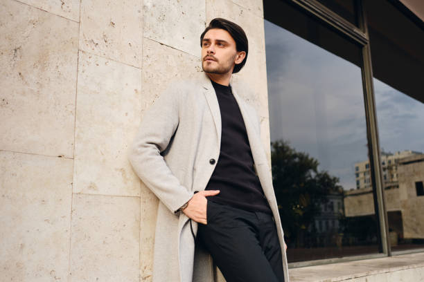 Young handsome stylish man in coat with hands in pockets intently looking away outdoor Young handsome stylish man in coat with hands in pockets intently looking away outdoor men fashion model stubble serious stock pictures, royalty-free photos & images