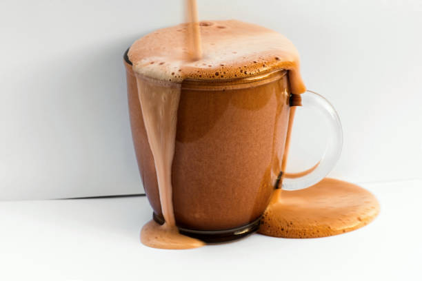 Overflowing frothy chocolate drink in glass on white background stock photo