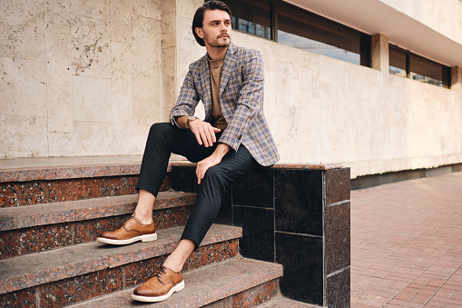 Young handsome stylish man in checkered jacket thoughtfully looking away sitting outdoor