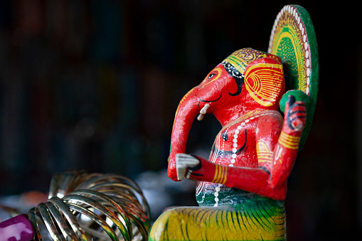 Close up photo of red and green colored Ganesha God icon of Hinduism. The background is black. Selective focus on icon.