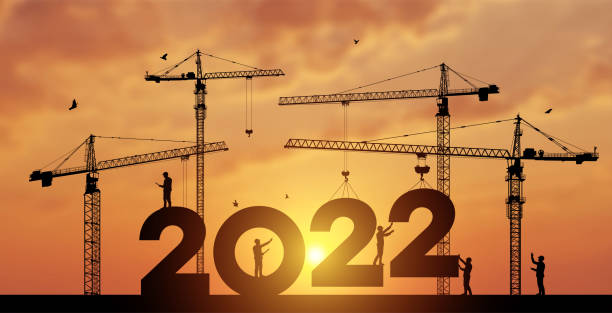 istock Black silhouette staff works as a to prepare to welcome the new year 2022. Large construction site, many construction cranes set vector numbers 2022. Construction team sets numbers for New Year 2022. 1357710390