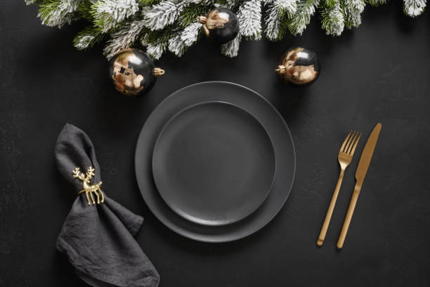 istock Christmas table setting with dark black plates, gold deer ring and gold cutlery. Golden gilded decorations. 1357711089