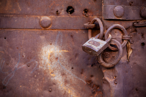 Close up photo of rusty padlock on weathered rusty metal door. No people are seen in frame. Shot with a full frame DSLR camera.