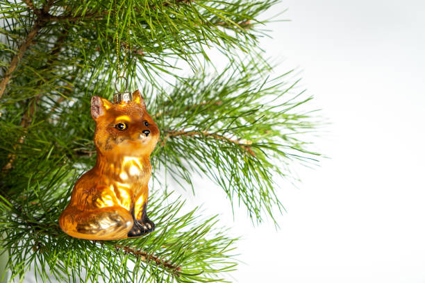 Glass Christmas tree toy red fox with glitter hangs on the branches of a New Year tree on a white background. Copy space or place for text. The basis for a postcard or congratulations.