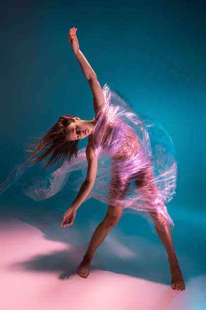 istock Solo performance. Beautiful flexible contemp dancer dancing with fabric isolated on gradient blue white background in neon light 1357716238