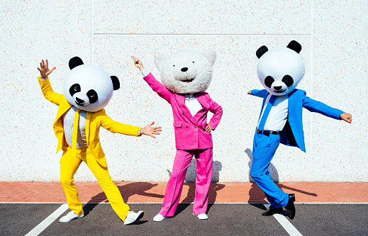 Group of friends wearing giant panda head and colored suits. Man and woman making party in a parking lot.