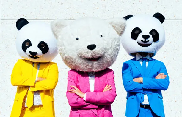 Group of friends wearing giant panda head and colored suits. Man and woman making party in a parking lot.
