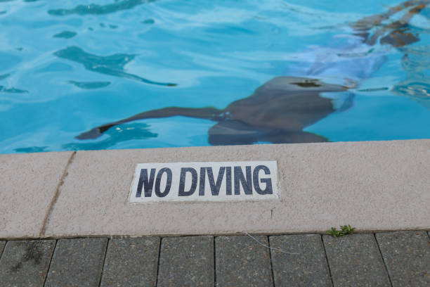 A no diving sign by a swimming pool with a black African-American man swimming stock photo