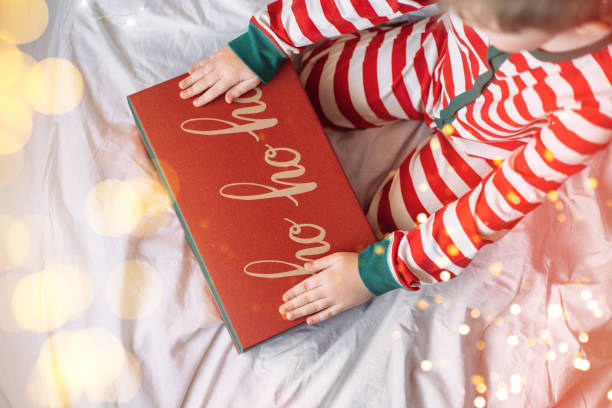 istock Child in striped pajamas put his hands on box with gift on white bed with superimposed lights 1357724270