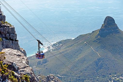 Cable Car travelling with Lion's Head in background from table Mountain, Cape Town, Cape Province, South Africa. South Africa on the southern tip of Africa is a beautiful, colourful and diverse country of varied landscapes from craggy rocky cliffs and coastline to savannah grasses of the natural wildlife parks that reflect the chequered social history and social issues of the country.