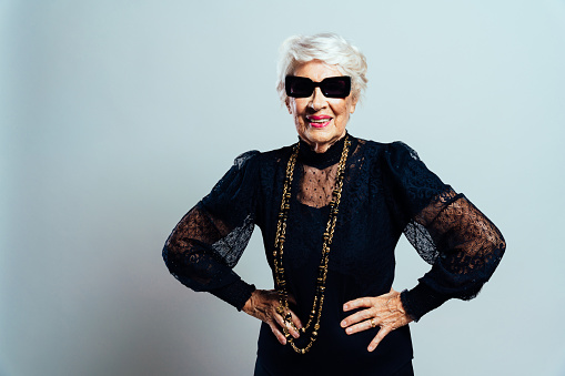 Beautiful and elegant old influencer woman. Cool grandmother posing in studio wearing fashionable clothes. Happy senior lady celebrating and making party. Concept about seniority and lifestyle