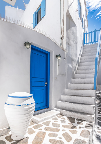 White wall with outdoor stairs and blue door on Mykonos Island in Greece.