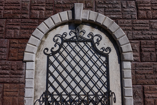 A metal lattice with an ornament on the arched opening of a closed window. The walls are tiled with brown stone tiles.