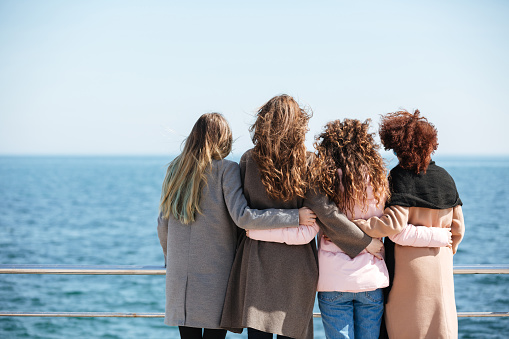 Back view of four friends hugging near sea