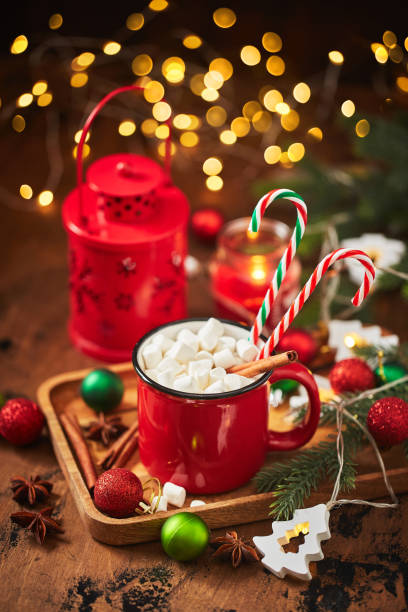 red cup of hot cocoa with marshmallows and candy canes on wooden table with christmas tree and glowing garland for christmas - julfika bildbanksfoton och bilder