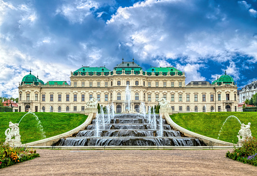 Belvedere Baroque palace in Vienna seen from the public gardens with fountains and dark clouds above.