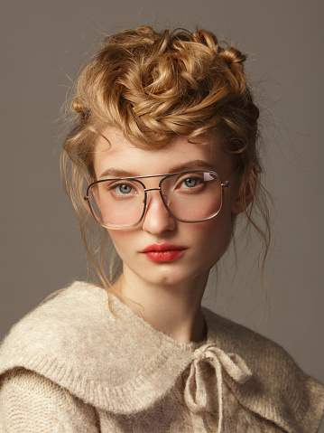 Portrait of young beautiful woman with eyeglasses and wearing knitted beige sweater, retro style