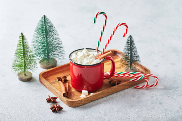 istock Red cup of hot cocoa with marshmallows and candy canes on with christmas tree 1357736209