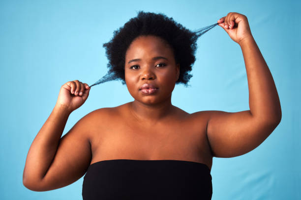 studioaufnahme einer schönen jungen frau, die strähnen ihrer haare zieht - overweight headshot studio shot looking at camera stock-fotos und bilder