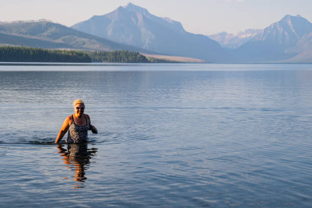 blonde adult woman enjoys taking a dip in the cold waters of lake mcdonald in glacier national park during a heatwave - montana mountain mcdonald lake us glacier national park imagens e fotografias de stock
