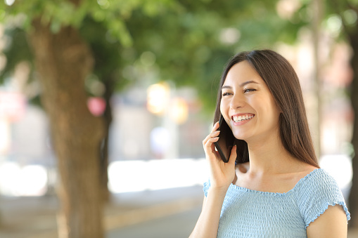 Happy asian woman talking on phone in the street