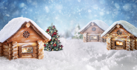 Fabulous Christmas composition with wooden houses and Christmas tree on a snowy winter day. Winter or Christmas panoramic background or greeting card.