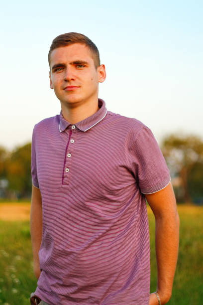 歩いている人たち。夏の日に自然の背景に屋外に立っている紫色のポロシャツを着た深刻な若いブルネットの男性の肖像画。20年代の男。ミレニアル世代。外。悲しい人 - 20s 20 25 years beauty beautiful ストックフォトと画像