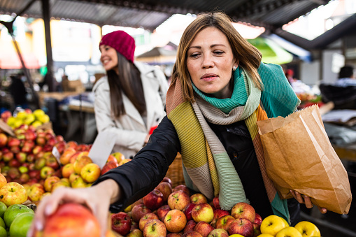 A mid-adult woman is shopping for organic apples at the farmer's market
