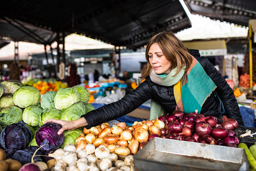 A mid-adult woman is shopping for cabbage at the farmer's market